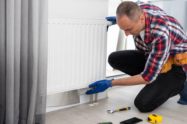Plumber in plaid shirt fixing radiator with tools nearby