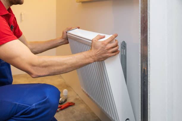 Technician installing or adjusting a white radiator heating system