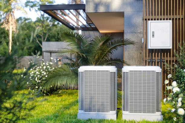 Two white air conditioning units in a lush garden next to modern building