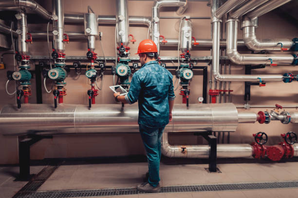 Worker in hard hat checks industrial piping system with tablet