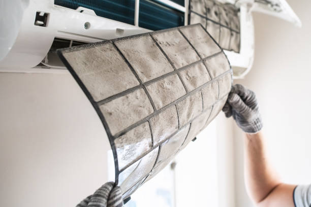 Dusty air conditioner filter being cleaned or replaced by gloved hand