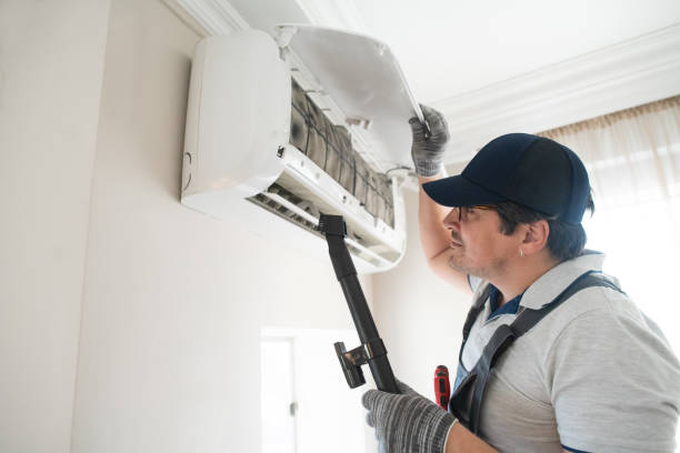 Technician in cap inspecting and cleaning wall-mounted air conditioning unit