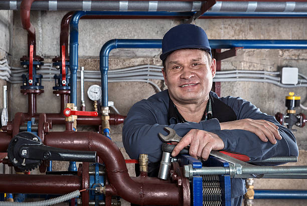 Smiling plumber with wrench standing near industrial pipes and valves