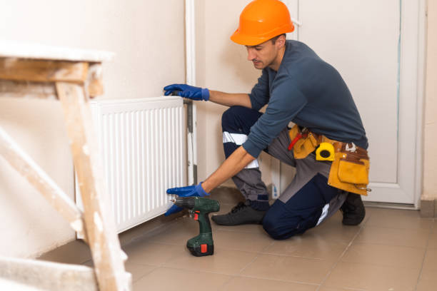 Worker in hard hat installing radiator with power drill and tools