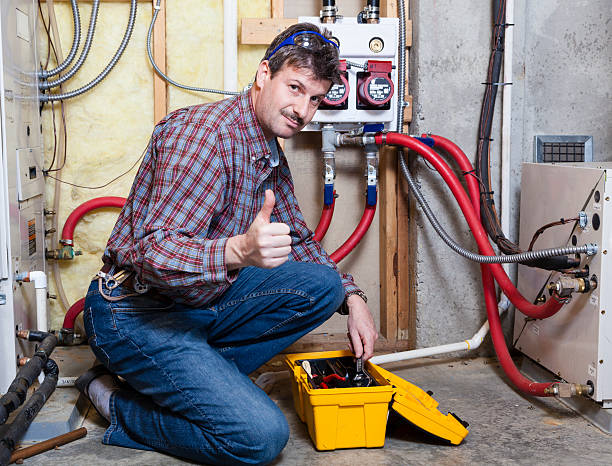 Plumber giving thumbs up next to pipes and electrical equipment