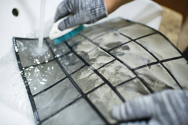 Gloved hands cleaning tiled surface with water and scrubbing