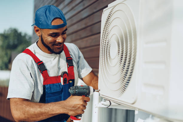 Worker in overalls installing or repairing an outdoor air conditioning unit