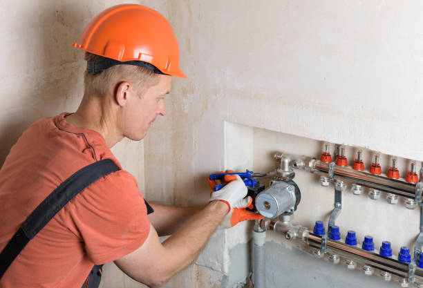 Plumber in orange helmet installing pipes on heating manifold system