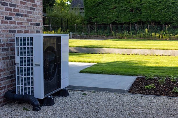 Modern heat pump installed beside brick wall with manicured backyard garden