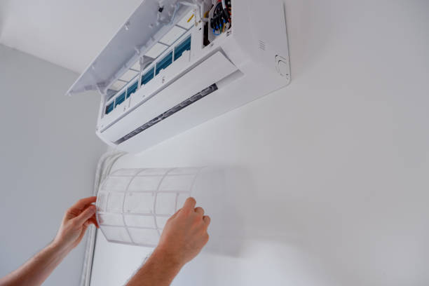 Hands installing or cleaning a white wall-mounted air conditioning unit