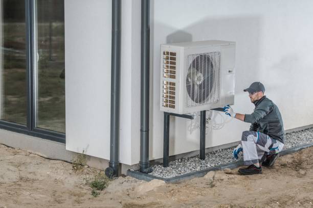 Technician inspecting outdoor air conditioning unit next to building