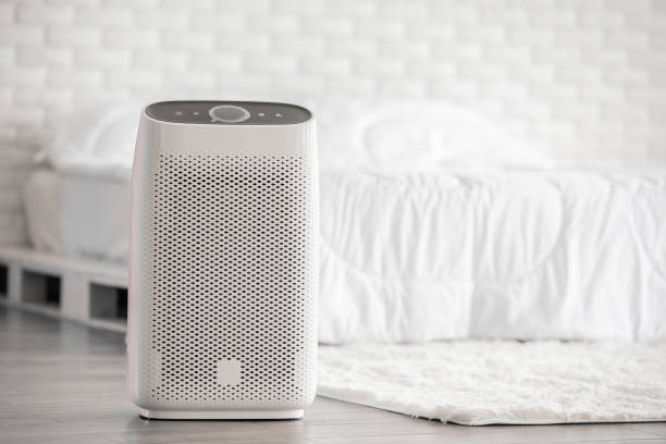 White air purifier placed on floor near bed in minimalist bedroom