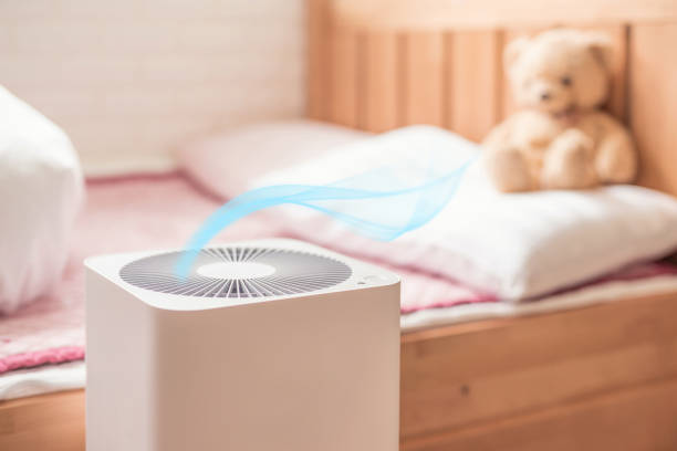 Air purifier with blue airflow on wooden bed with teddy bear in background
