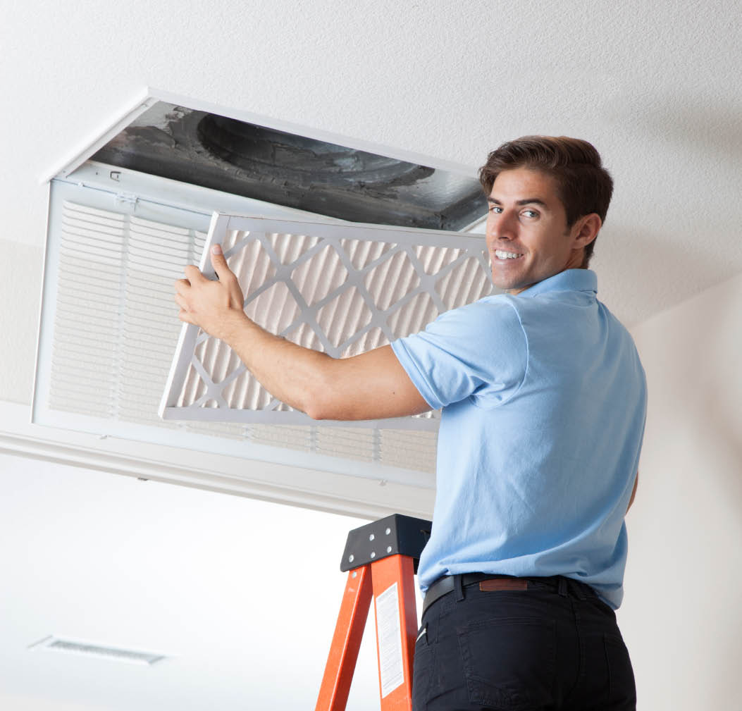Technician on ladder replacing air filter in ceiling vent