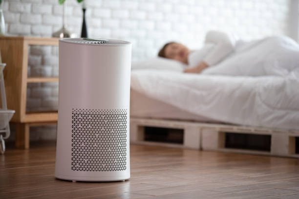 Air purifier on floor near bed with sleeping person in background