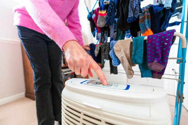 Person operating dehumidifier near colorful laundry hanging on drying rack