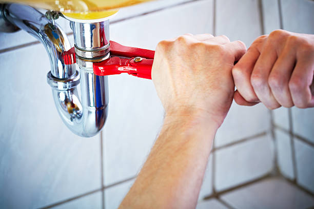 Hands using a wrench to tighten plumbing pipe under a sink