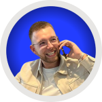 Homme souriant portant des lunettes et une chemise claire, parlant au téléphone sur un fond bleu circulaire.