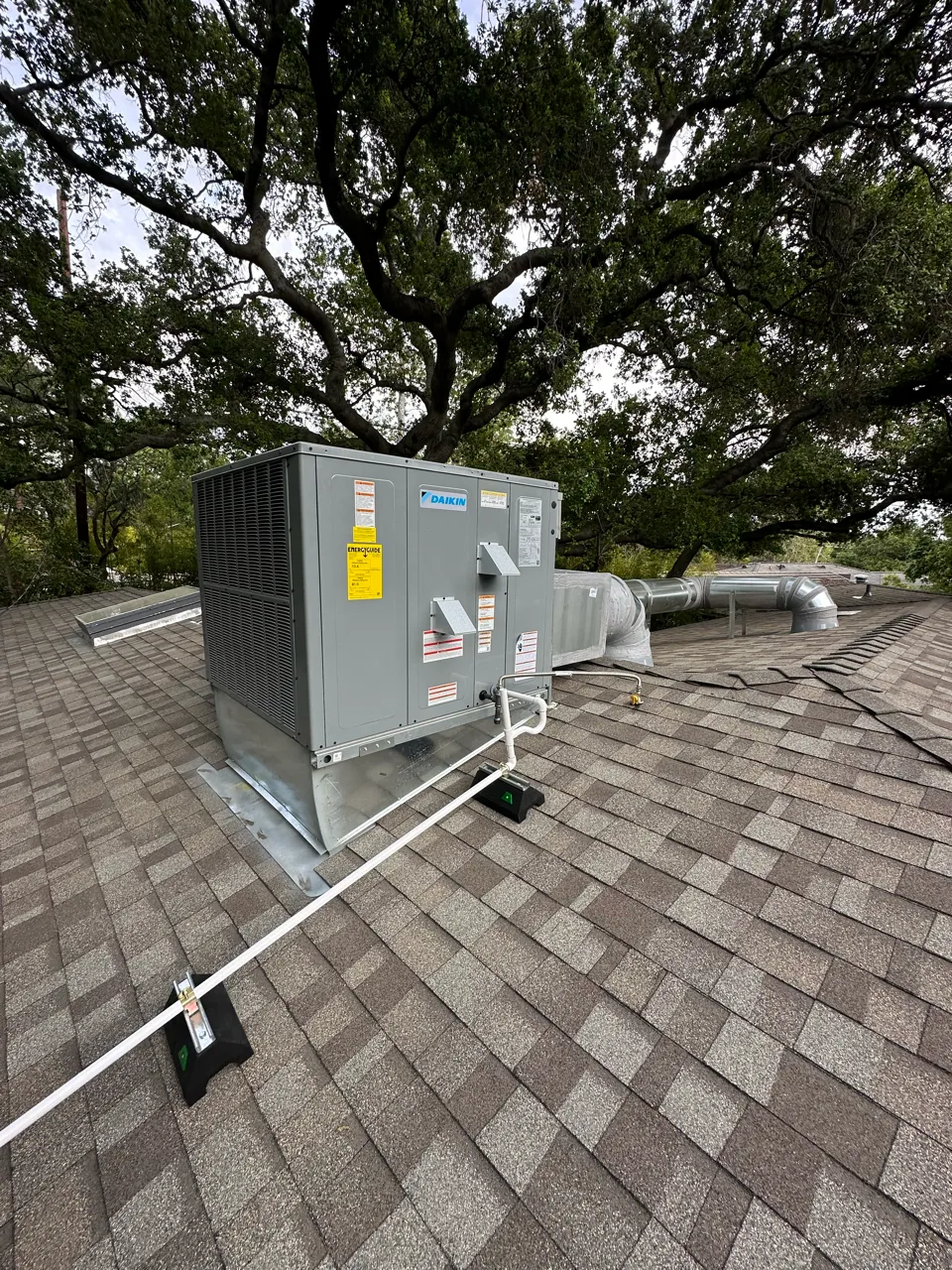 Daikin HVAC unit installed on a shingle roof with trees in background