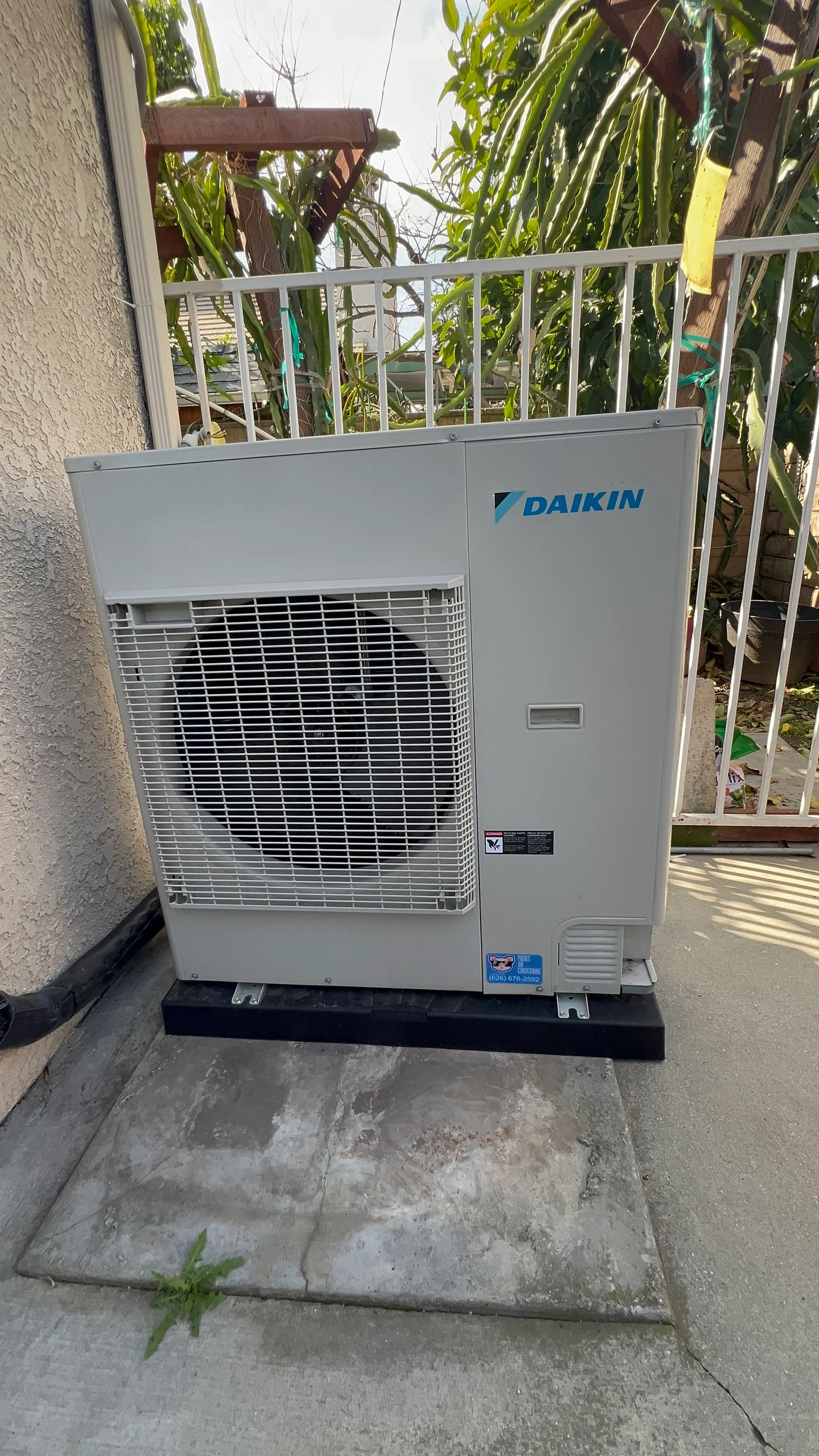 Daikin air conditioning unit installed on concrete pad near white railing