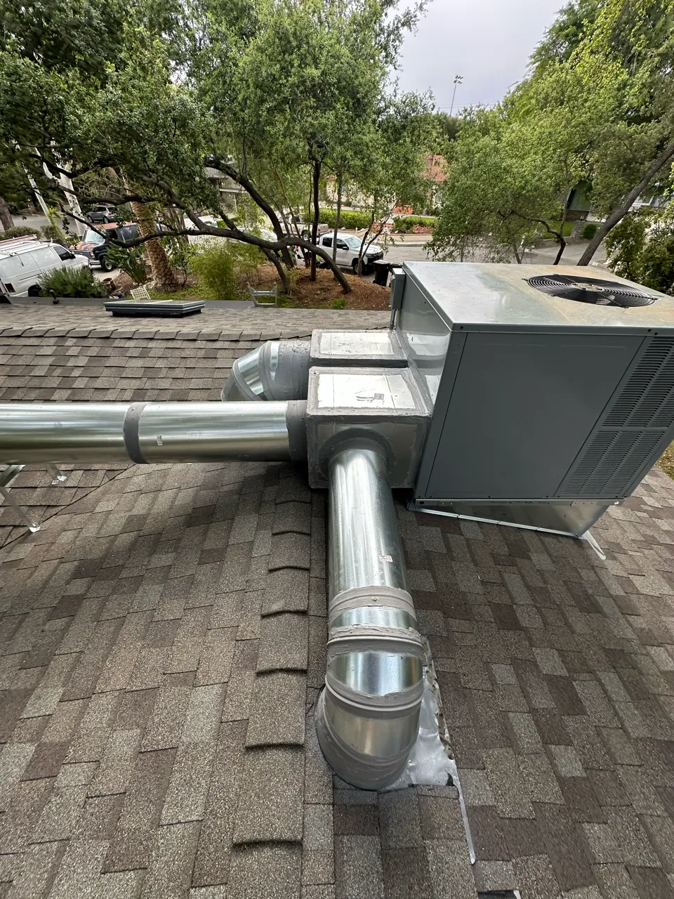 Silver HVAC ventilation pipes and unit on residential roof with trees