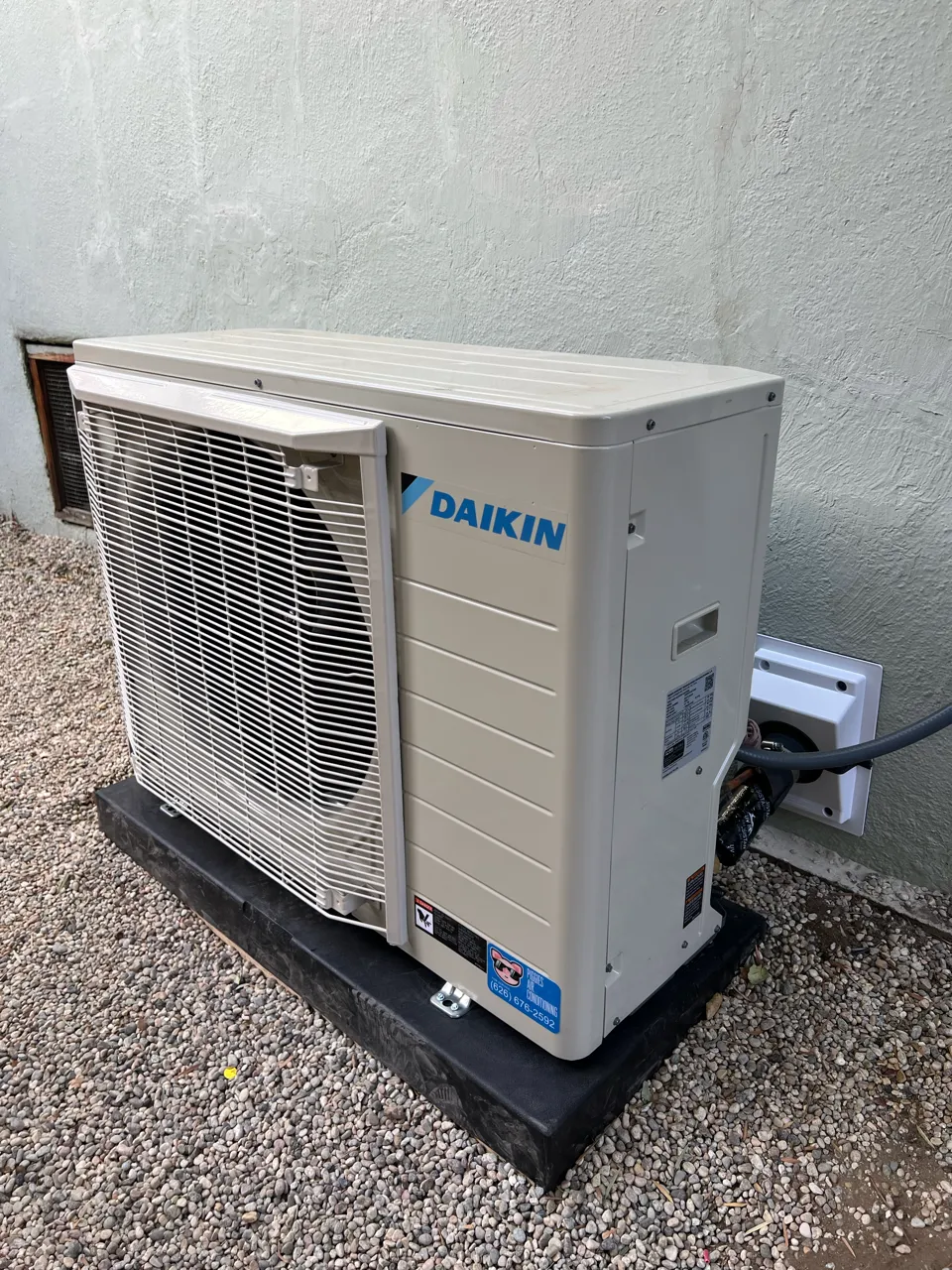 Daikin air conditioning unit installed on gravel outside a textured wall