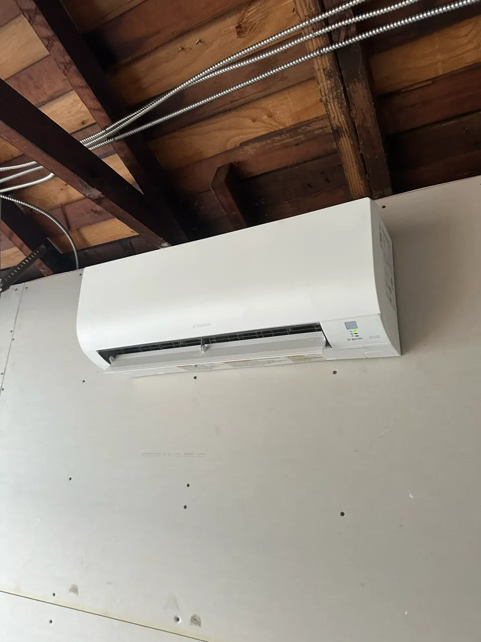 White ductless mini-split air conditioner mounted on white wall with wooden ceiling
