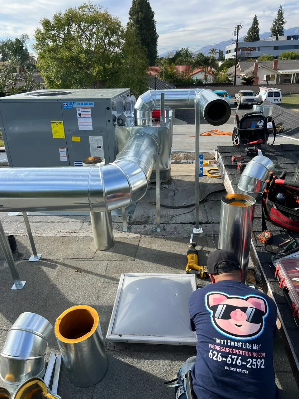 HVAC technician installing large metal ductwork and Daikin air conditioning unit