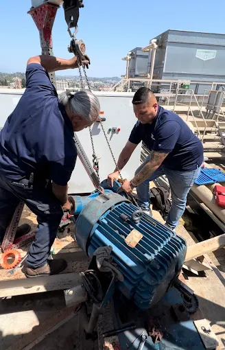 Workers using crane to move heavy industrial electric motor on rooftop