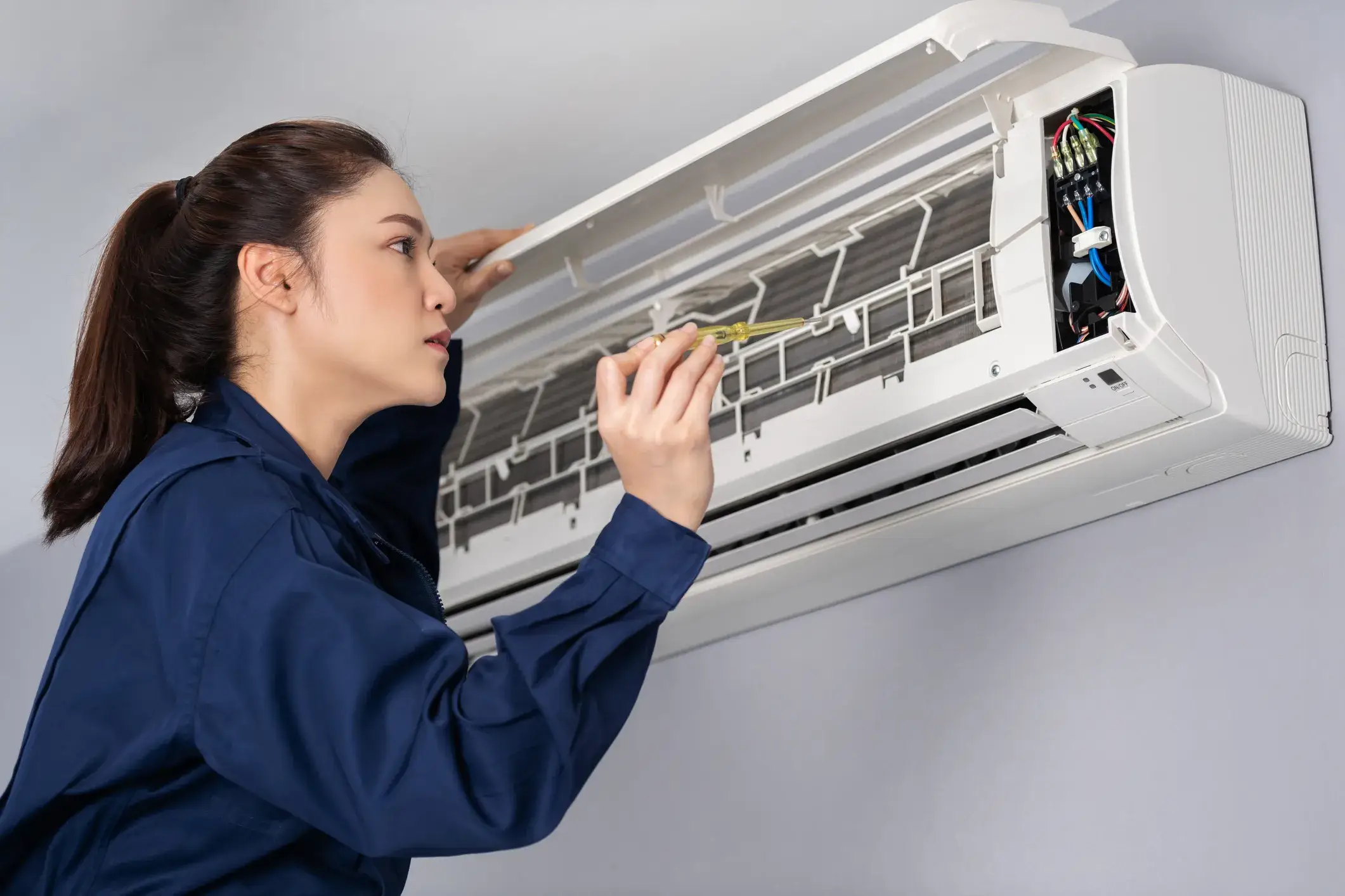 Female HVAC technician servicing an indoor air conditioning unit with a screwdriver.