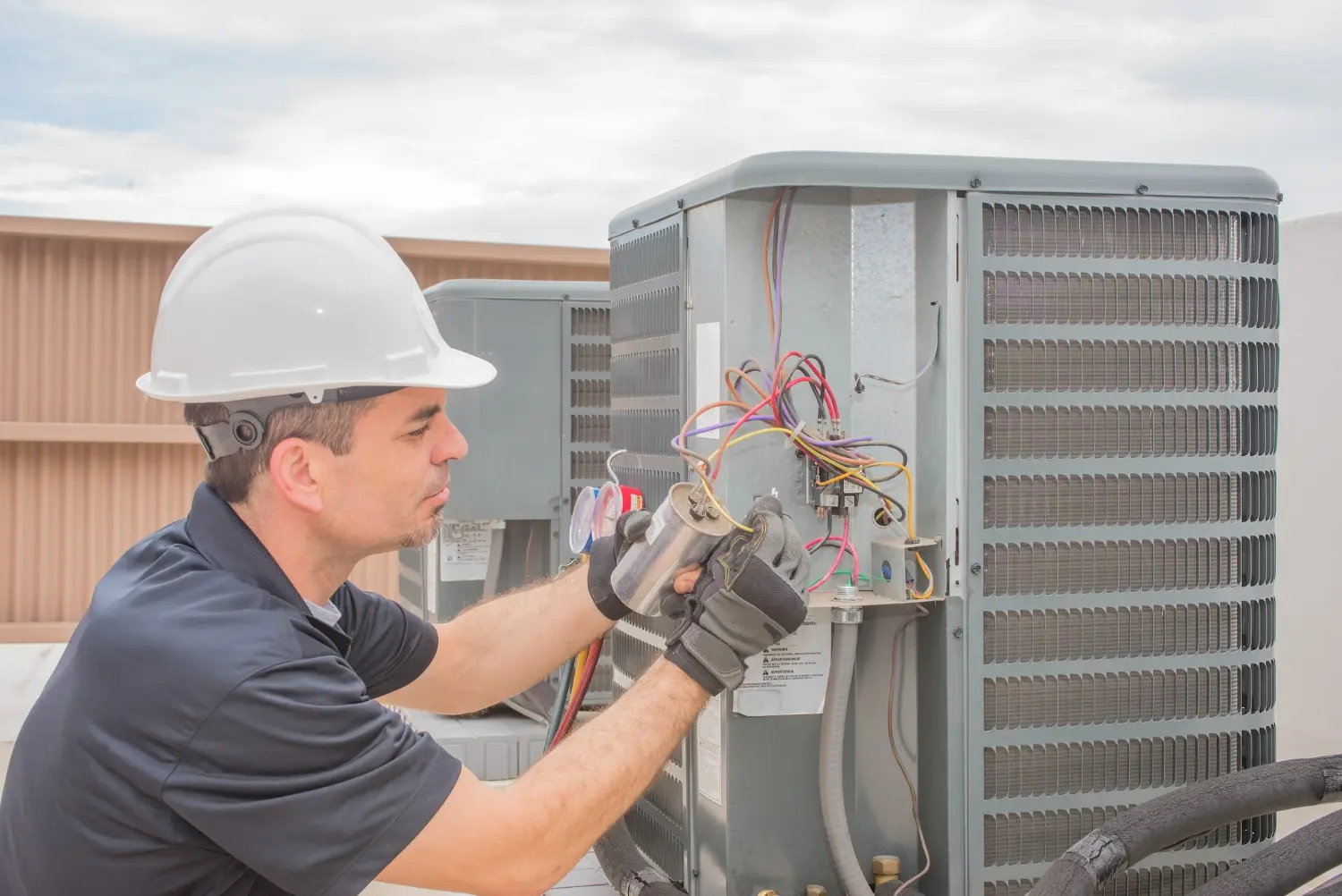 A technician in a hard hat and gloves performs commercial AC repair on a rooftop unit by handling an electrical component.