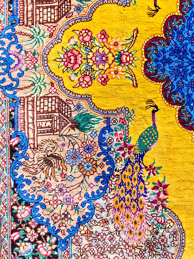 Kleurrijk wandtapijt met pauwontwerp en bloemmotieven op geel-blauwe achtergrond.