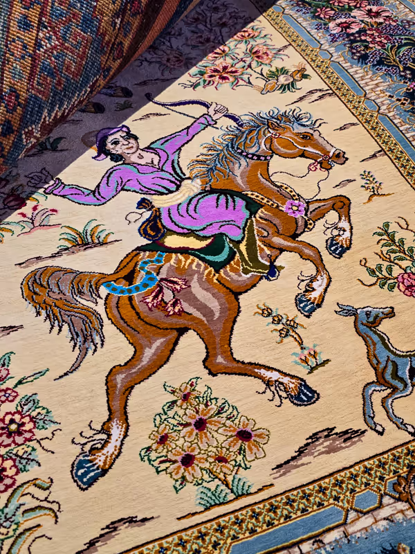 Kleurrijk tapijt met een gedetailleerde afbeelding van een persoon op een paard, omringd door bloemenpatronen.