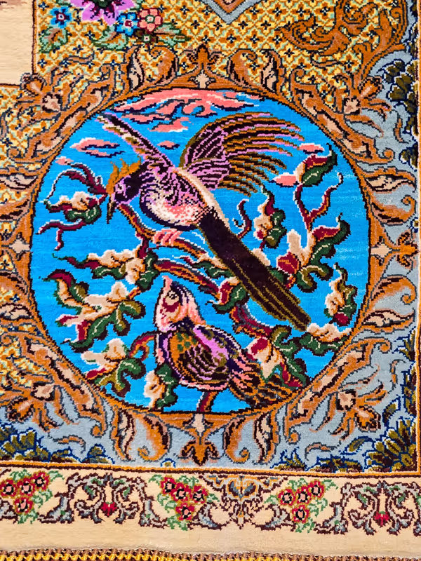 Een gedetailleerd wandtapijt toont twee kleurrijke vogels omringd door takken in een cirkelvormig patroon.