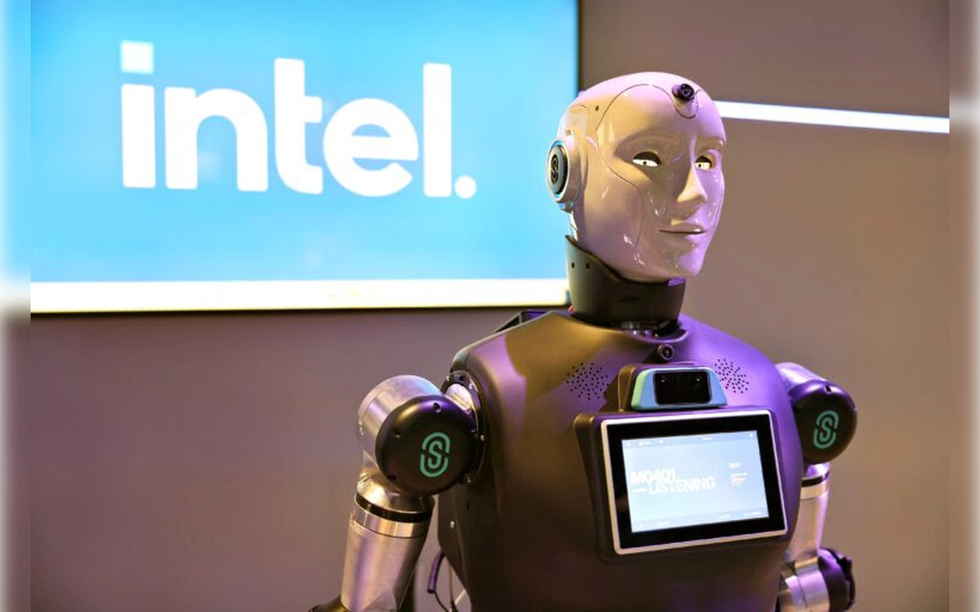 Ein humanoider Roboter mit weißem Kopf und mechanischem Oberkörper vor einem leuchtenden Intel-Logo. Auf seiner Brust befindet sich ein Display mit Statusanzeigen.
