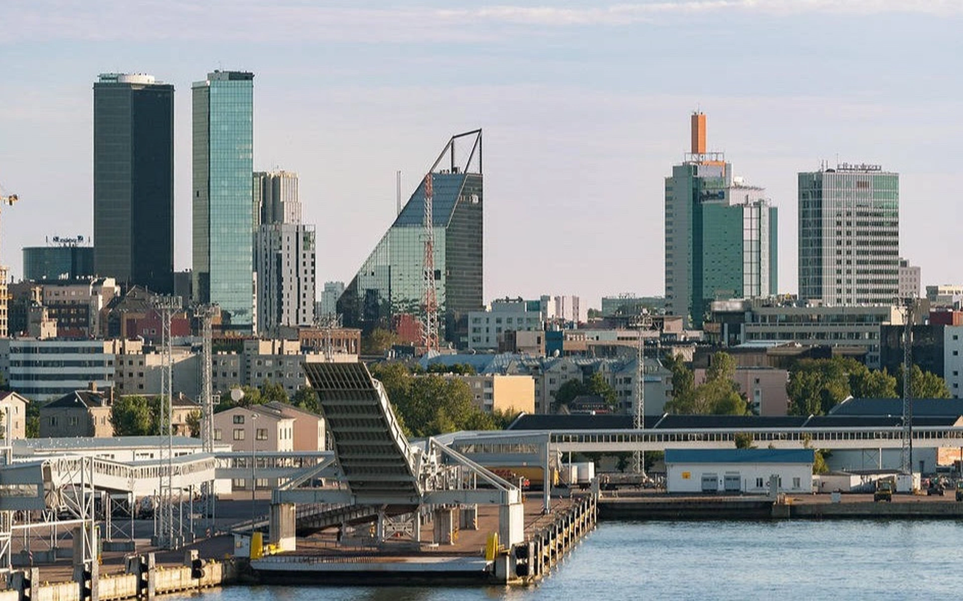 Moderne Skyline von Tallinn an der Küste mit markanten Hochhäusern, Hafenanlagen und einer hochgeklappten Laderampe im Vordergrund bei Tageslicht.