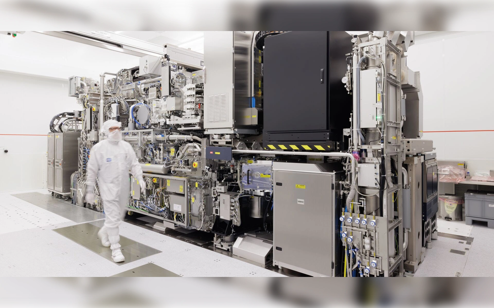 Mitarbeiter im weißen Reinraumanzug geht an einer hochkomplexen ASML-Lithografieanlage zur Chipherstellung vorbei.