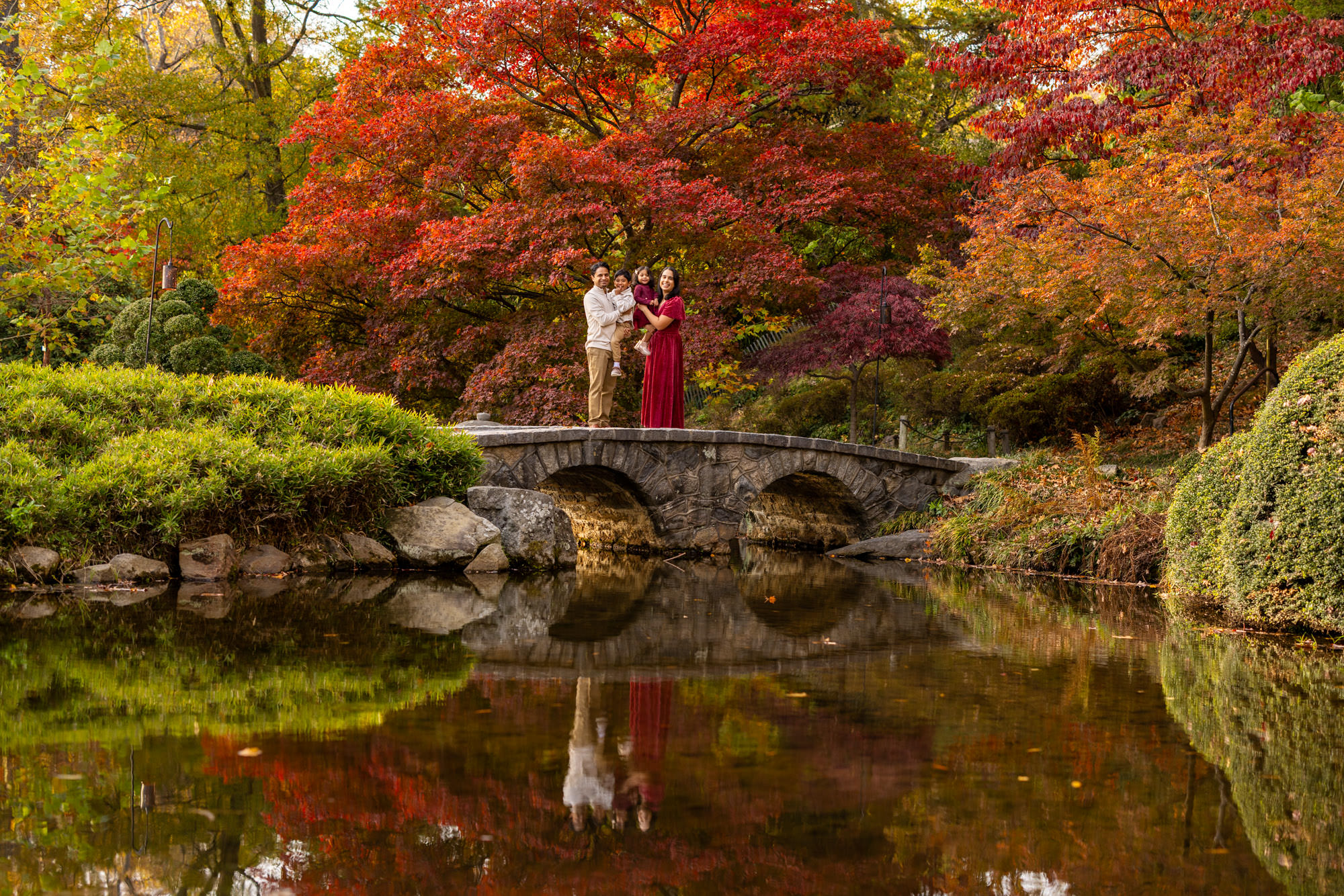 A family poses for a picture on a bridge in the Japanese Gardens in Maymont Park in Richmond, Virginia during peak fall foliage