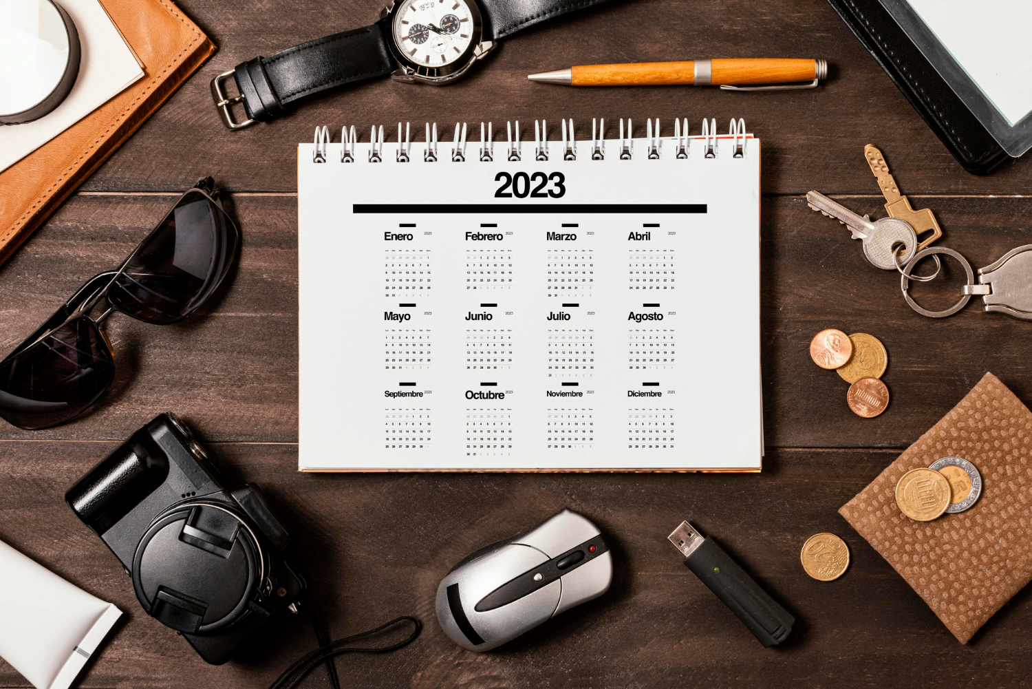 kaldanrz płasko na drewnianym stole, dookoła zegarek klucze okulary aparat dlugopis monety, bezpośrednie ujęci z góry