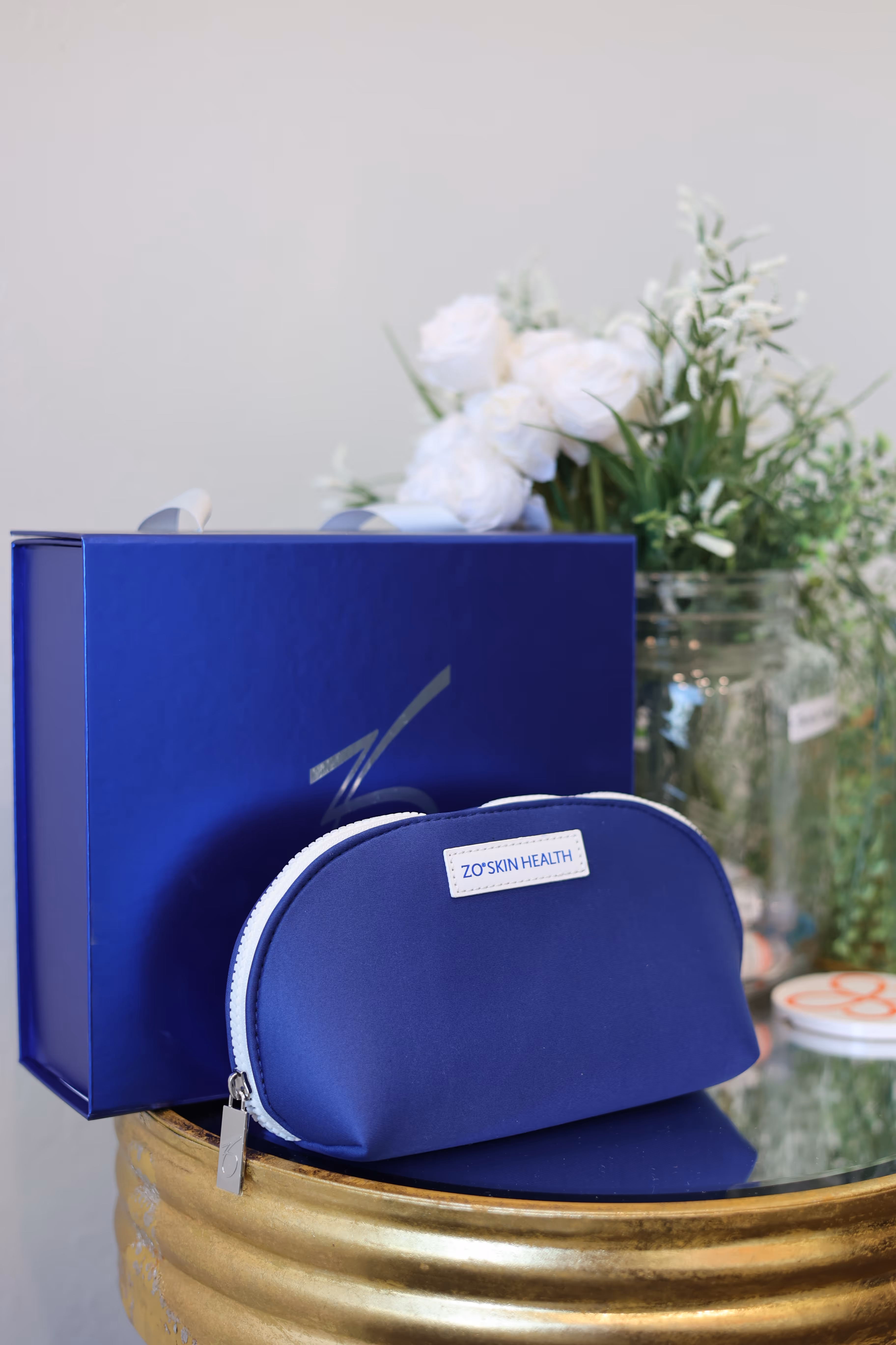 Woman in blue scrubs holding two blue skincare product boxes in front of shelves with similar products.