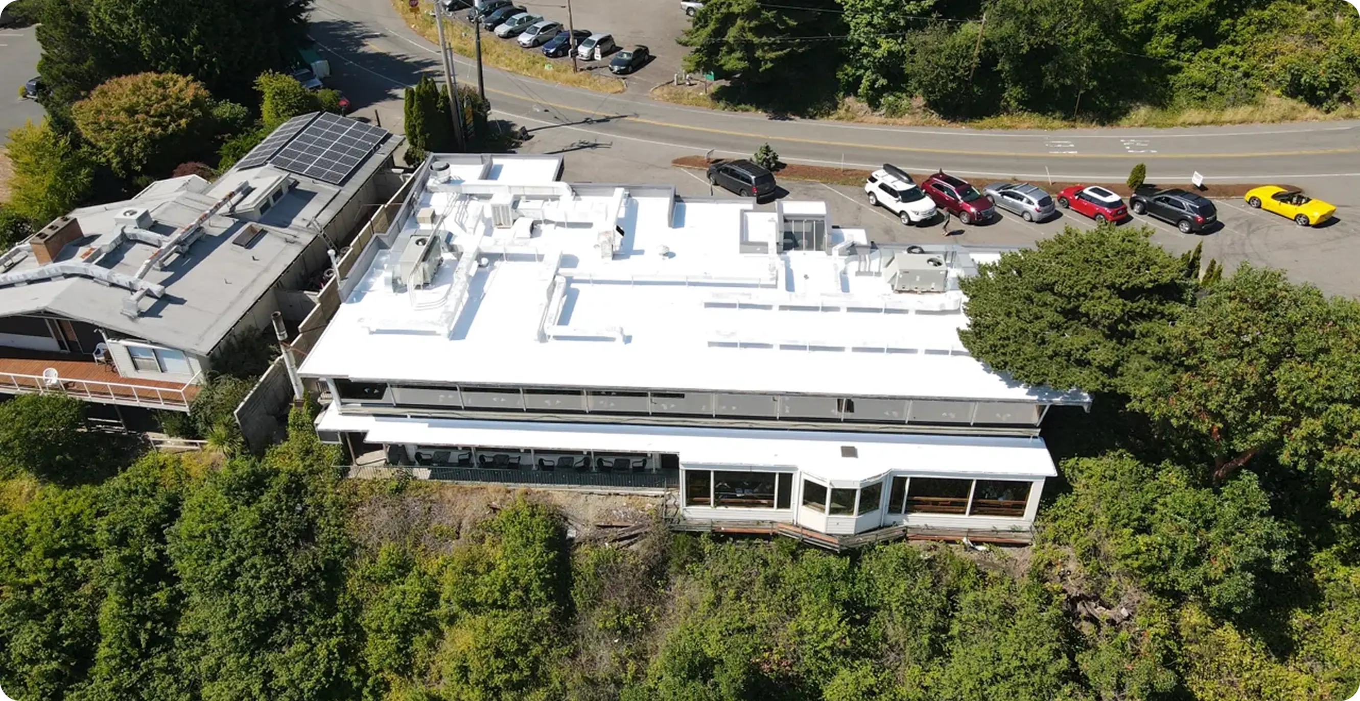Aerial view of completed flat roof restoration on commercial building surrounded by trees — new white membrane system installed for durability and energy efficiency.