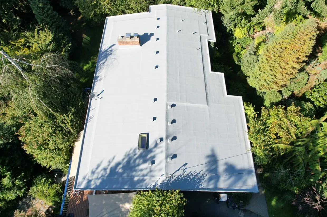 Drone view of restored flat roof on residential building surrounded by trees — clean gray membrane system installed for weather resistance and longevity.