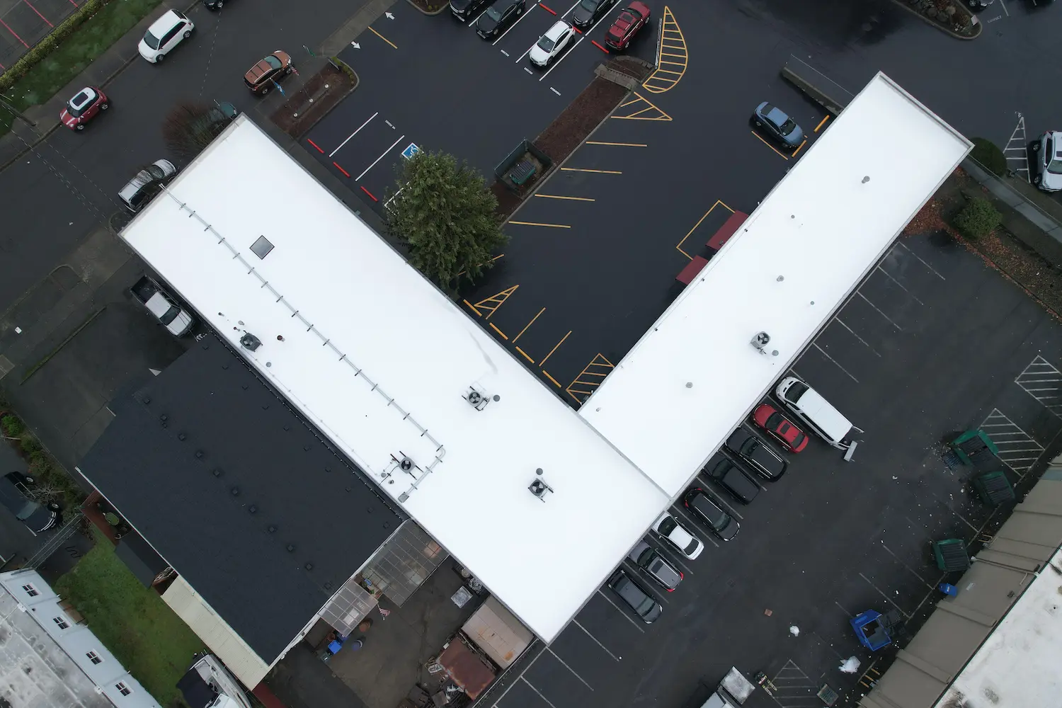 Flat roof restoration on L-shaped commercial building — new white membrane installed for improved waterproofing and energy performance.