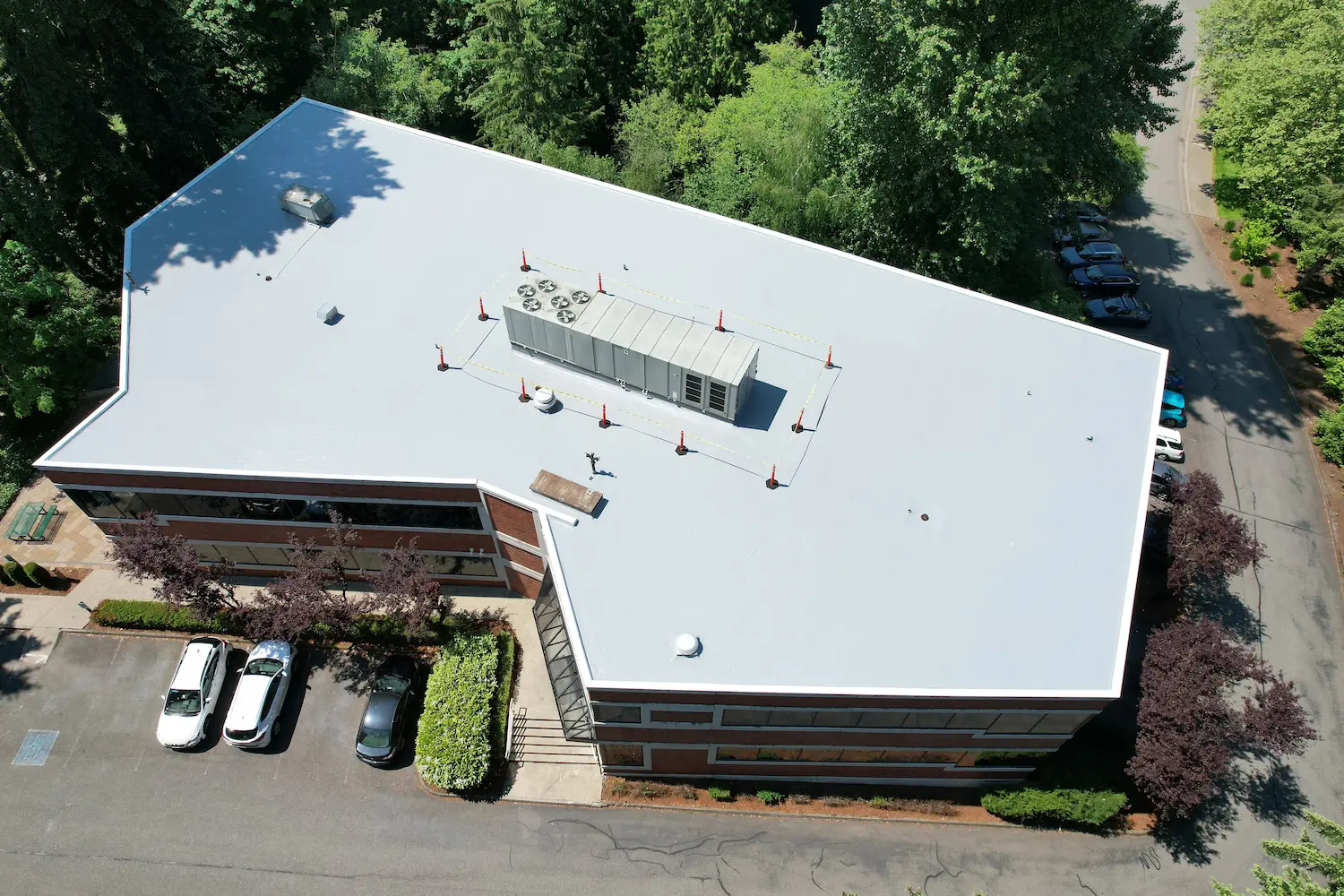 Flat roof restoration on two-story office building surrounded by trees — new gray membrane system installed to improve drainage, durability, and thermal performance.