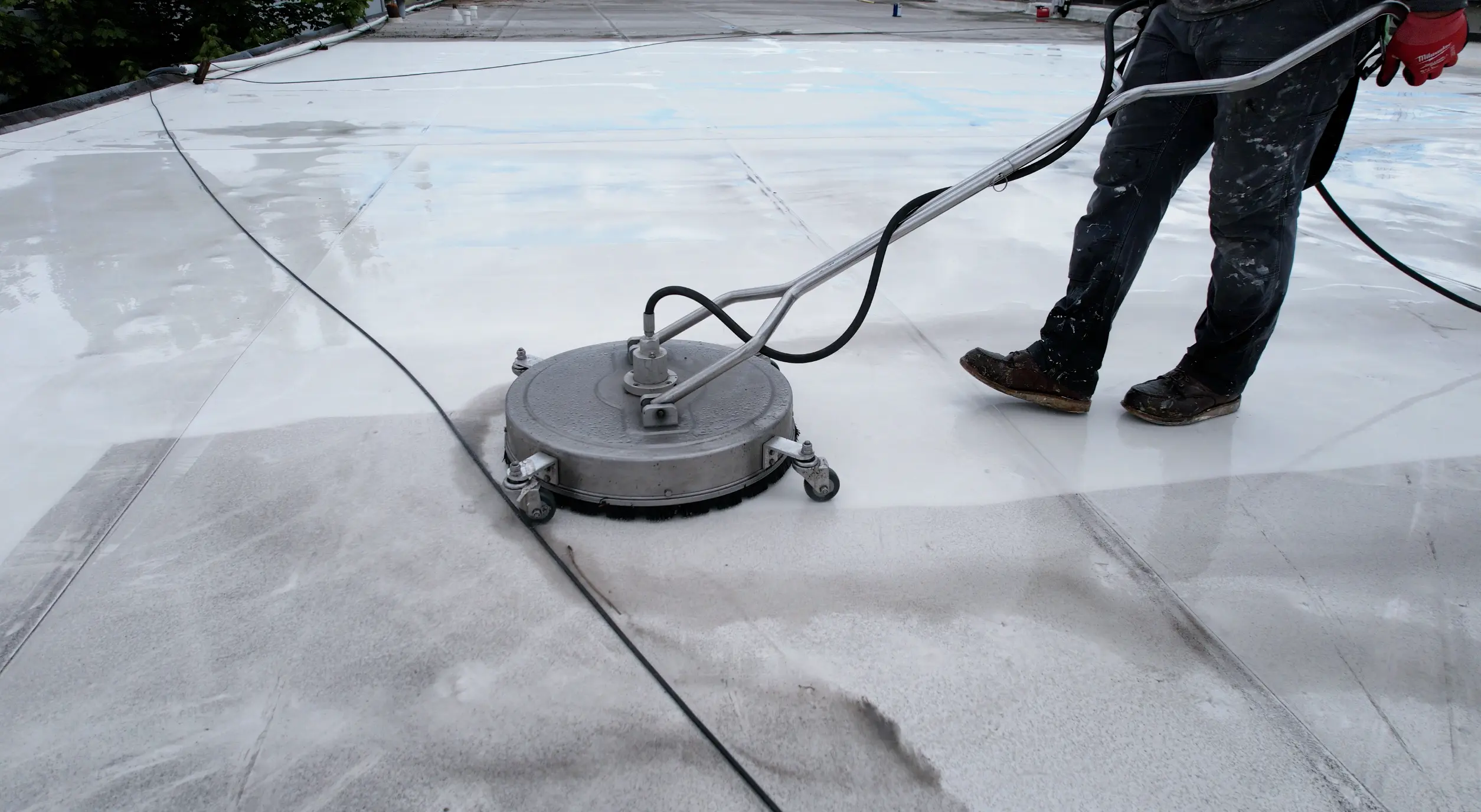 Low-pressure rotary surface cleaner used on flat roofing membrane — professional roof washing for safe, even cleaning of large roof areas.