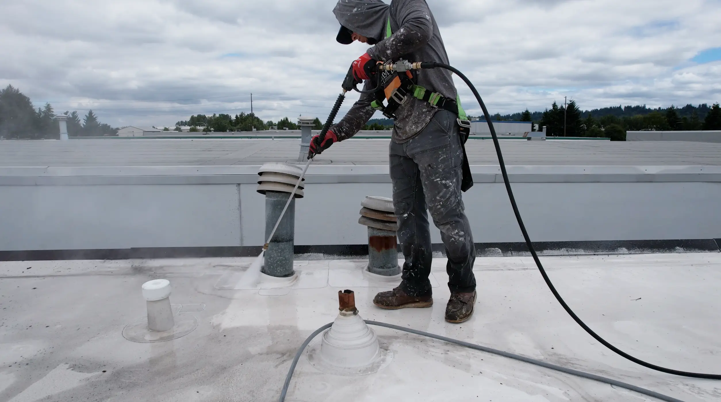 Commercial flat roof power washing in progress — Flat Roof Pros technician using hose and surface cleaner to remove grime and preserve roofing system.