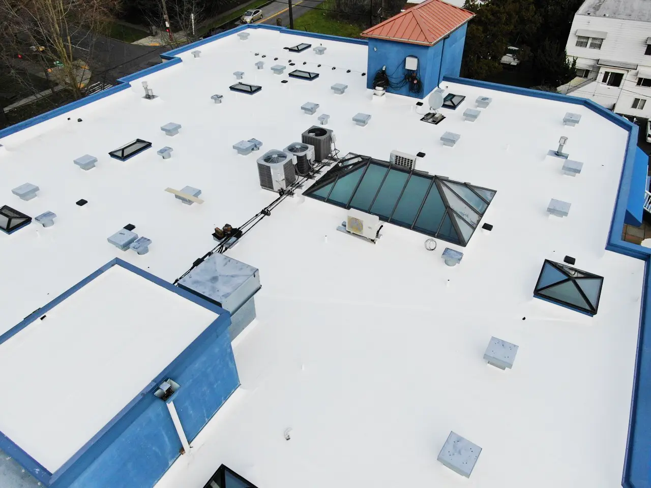 Newly restored white commercial flat roof with clean membrane, sealed skylights, and upgraded rooftop HVAC units on a multi-family residential building.