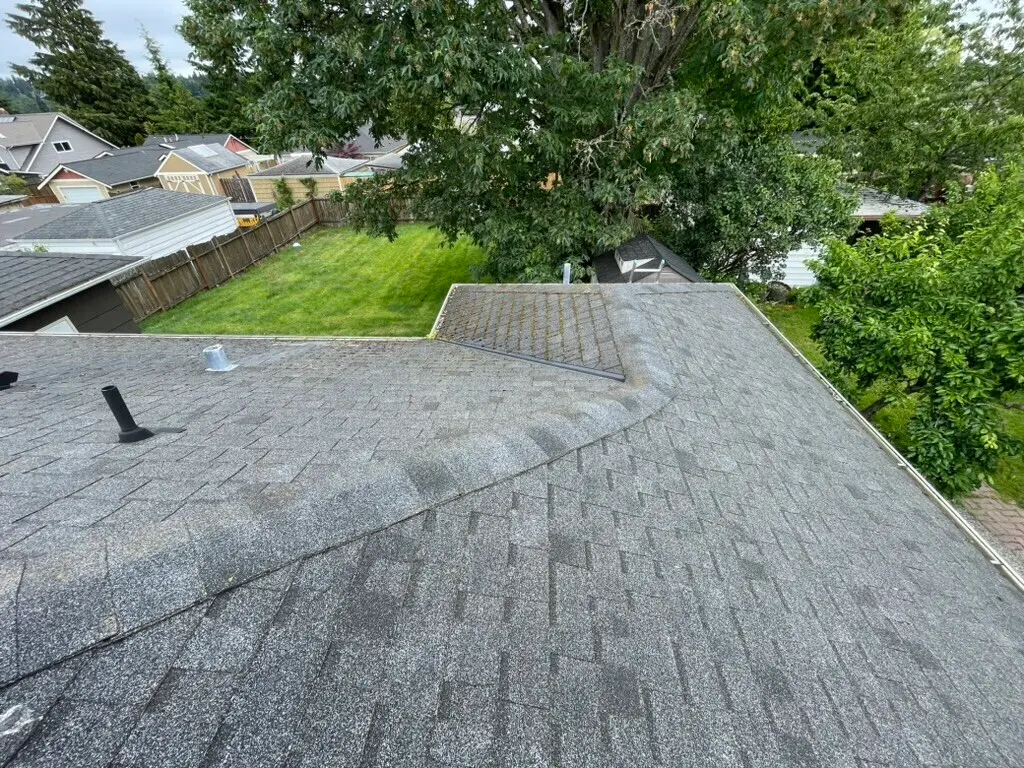 Worn asphalt shingle roof on a residential home with visible granule loss, vent pipes, and discoloration—potential candidate for roof inspection or replacement.