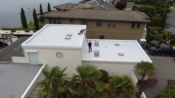 Residential flat roof with newly installed white PVC membrane in a lakeside neighborhood, featuring skylights, edge metal, and clean waterproofing details.