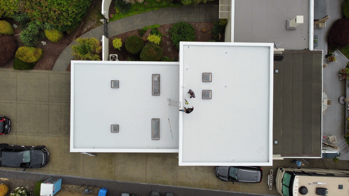 Top-down drone view of completed white PVC flat roof installation on a modern residential home, featuring skylights, clean seams, and upgraded waterproofing.